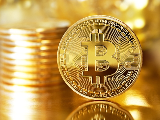 Золотая монета биткоин отражается в поверхности стола 