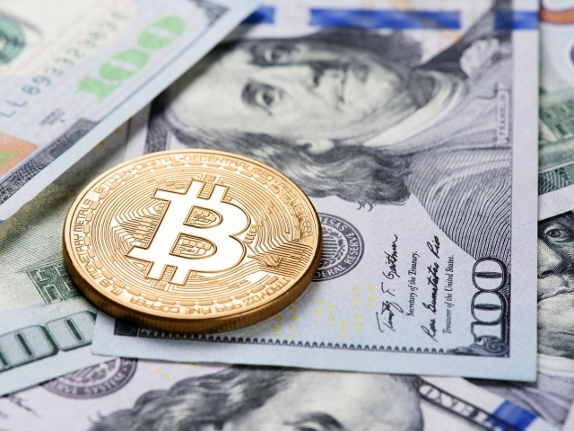 Золотая монета биткоин лежит на долларах 