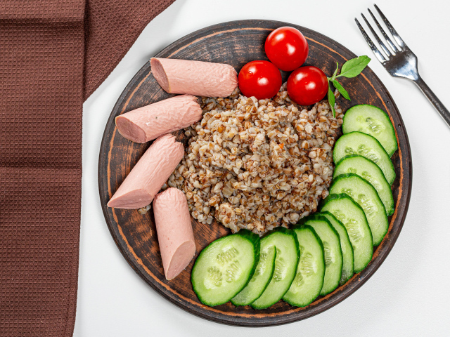 Гречка на тарелке с помидорами, огурцами и сосисками