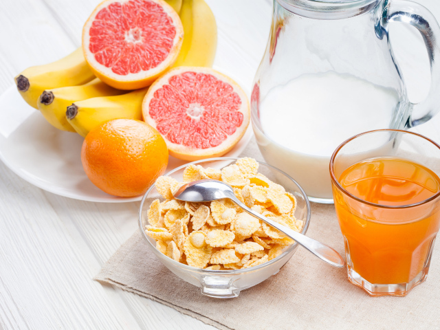 Кукурузные хлопья на столе с молоком, соком и свежими фруктами на завтрак