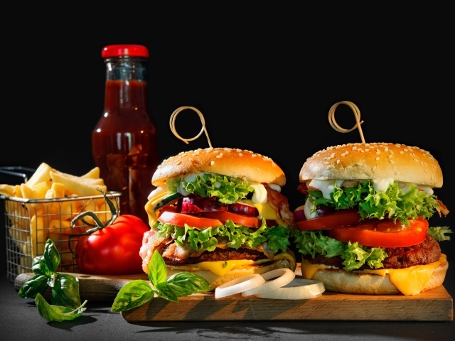 Гамбургеры на столе с картофелем и кетчупом на черном фоне