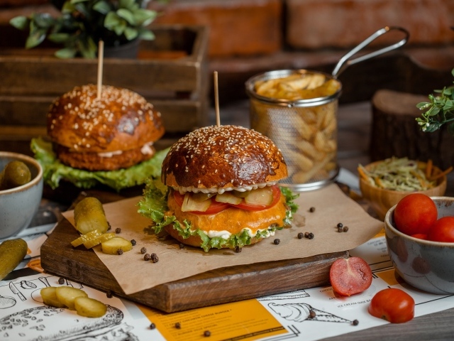 Гамбургеры на столе с помидорами, картофелем фри и солеными огурцами