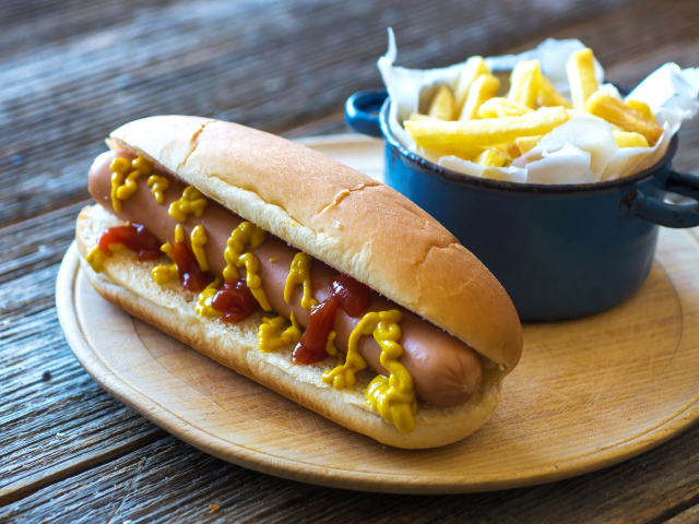 Хот дог с горчицей и кетчупом на столе с картофелем фри  