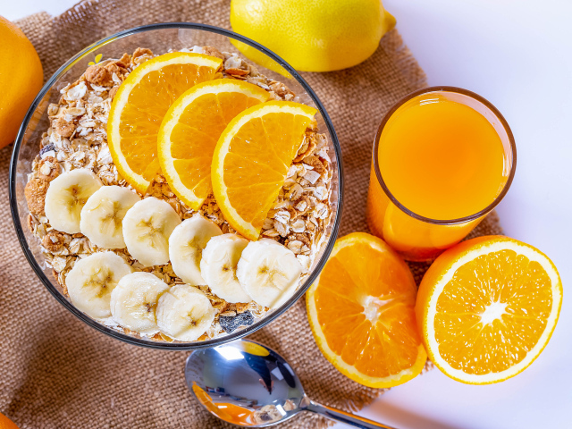 Овсяные хлопья в тарелке с кусочками банана и апельсина на столе с соком