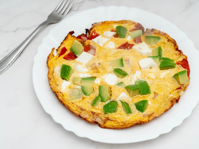 Омлет с авокадо и кусочками помидора на белой тарелке 