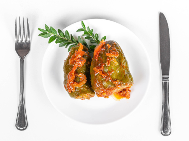 Фаршированный перец на белой тарелке со столовыми приборами