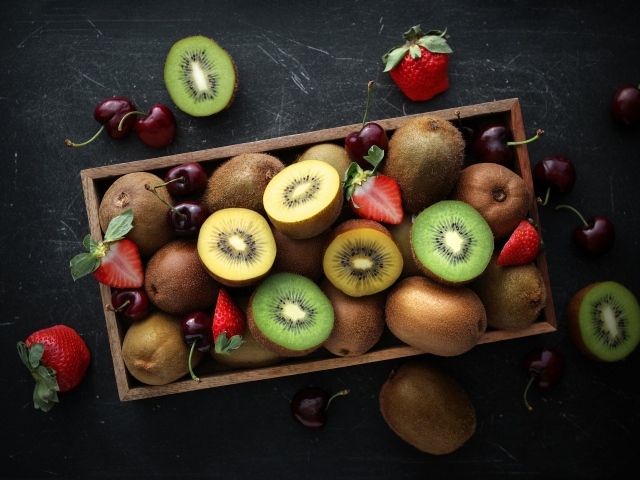 Ящик с киви, клубникой и черешней на столе 