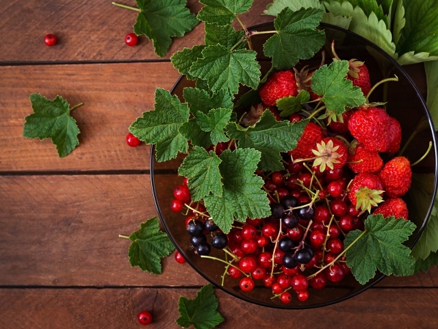 Ягоды смотродины в миске с клубникой и зелеными листьями
