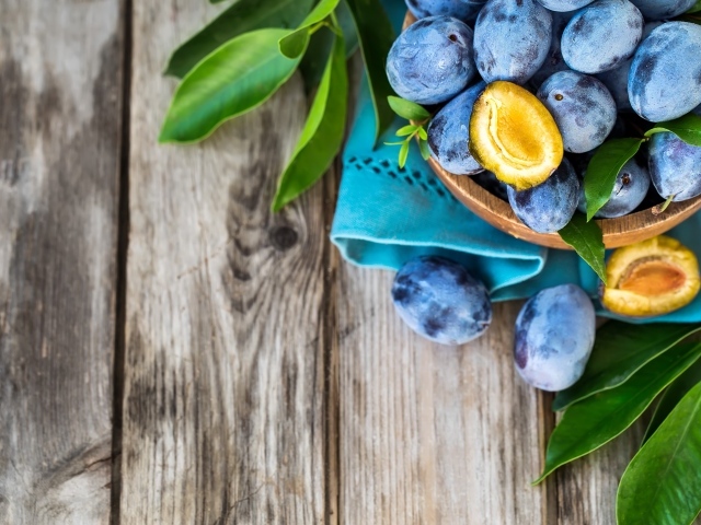 Свежие синие сливы с зелеными листьями на столе 