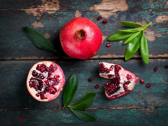 Большой спелый гранат на деревянном столе с зелеными листьями