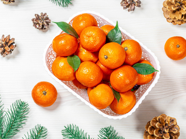 Много спелых мандаринов в белой корзинке на столе с шишками