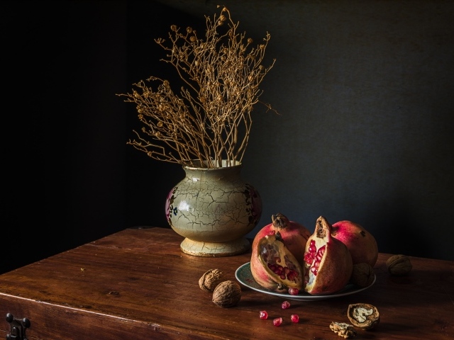 Красный гранат на столе с грецкими орехами и сухой веткой в вазе