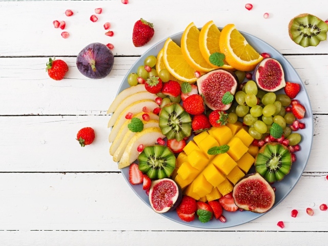 Вкусные сочные свежие фрукты и ягоды на тарелке на столе