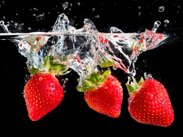 Три ягоды клубники в воде на черном фоне