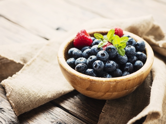 Мокрые ягоды черники в деревянной миске с малиной 