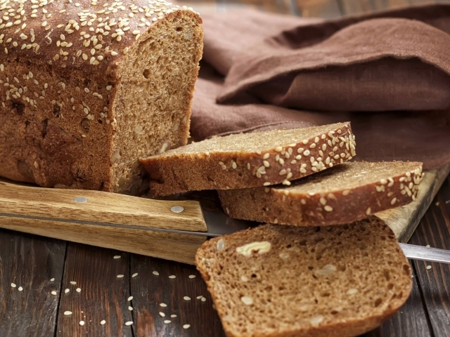 Буханка хлеба нарезанная кусочками на столе с ножом