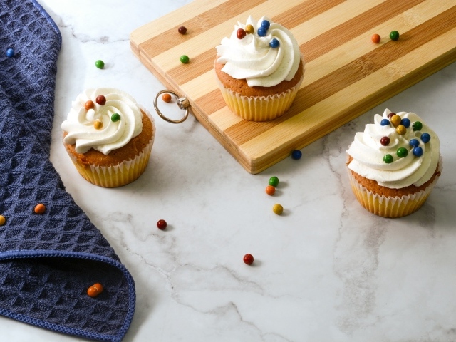 Кексы с кремом и разноцветными шариками на столе с доской