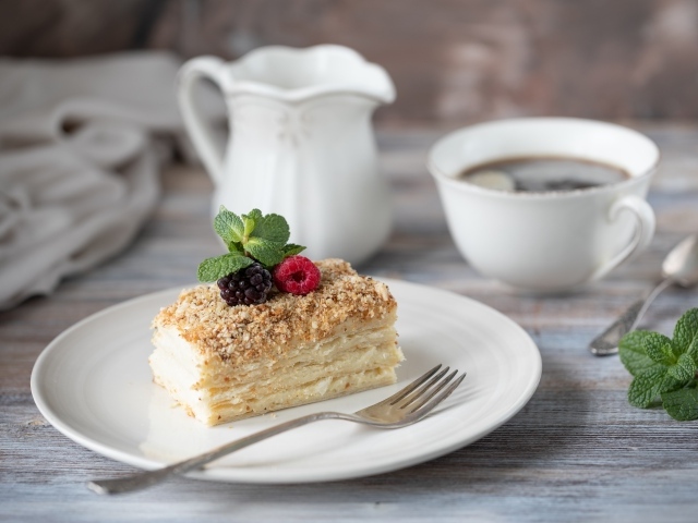 Кусок торта лежит на белой тарелке на столе с кофе