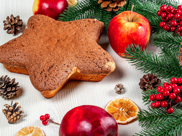 Рождественский кекс на столе с еловыми ветками,  яблоками и шишками