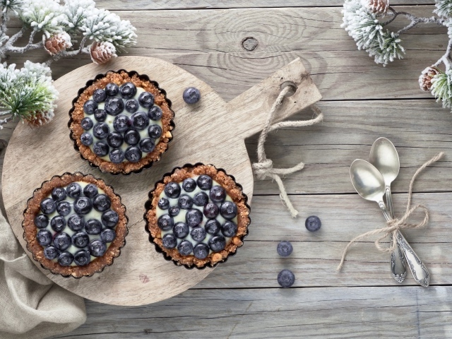 Кексы с кремом и ягодами черники на столе с чайными ложками