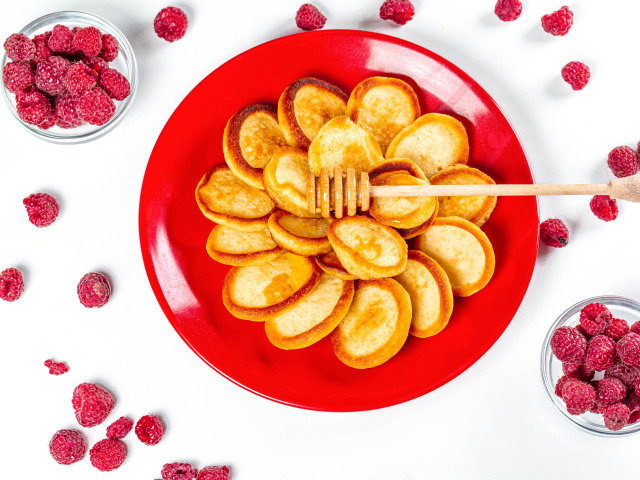 Оладьи на красной с медом на красной тарелке на столе с ягодами малины
