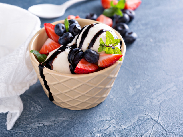 Шарики мороженого в стакане на столе с клубникой и ягодами черники