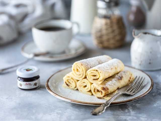 Блины на тарелке с сахарной пудрой на столе с кофе