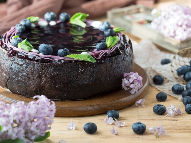 Пирог с джемом и ягодами черники на столе с сиренью 