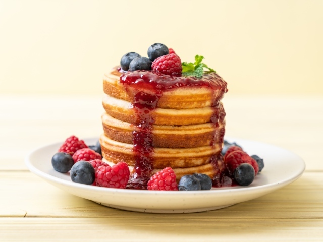 Румяные панкейки с джемом и ягодами черники и малины на тарелке