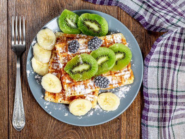 Сладкие вафли на тарелке с сахарной пудрой, бананами и киви