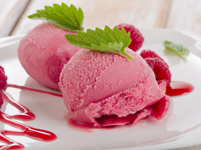 Два шарика малинового мороженого на тарелке с ягодами 