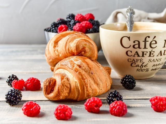 Два круассана на столе с чашкой кофе и ягодами
