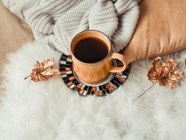 Чашка кофе стоит на покрывале с теплым свитером 