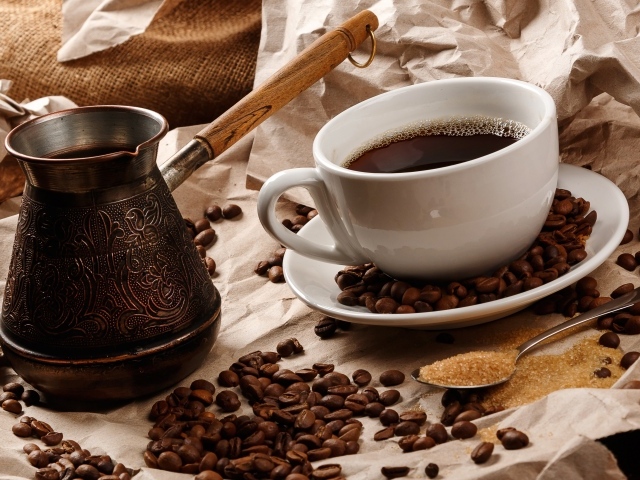 Чашка горячего кофе на столе с туркой, зернами и коричневым сахаром
