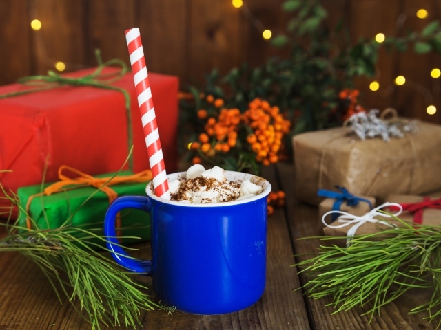 Синяя чашка горячего шоколада с маршмеллоу на столе с еловыми ветками и подарками