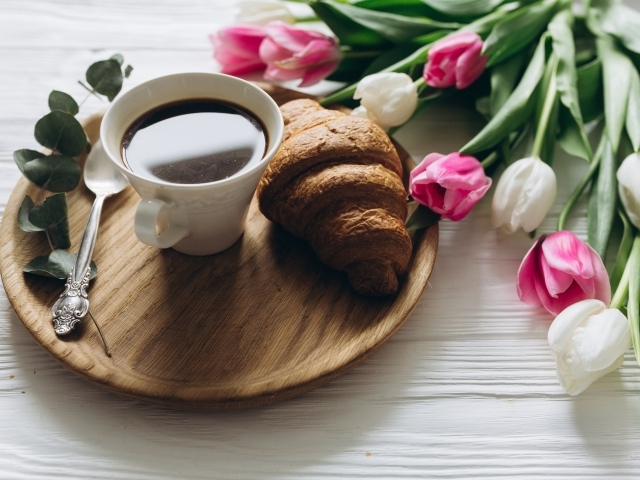 Чашка кофе и круассан на столе с букетом тюльпанов