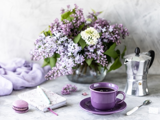 Чашка кофе на столе с блокнотом и букетом сирени в вазе