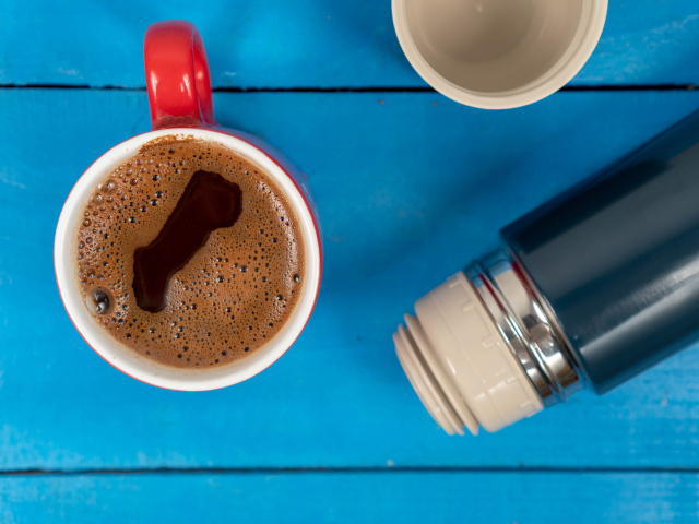 Красная чашка кофе с термосом на голубом столе 