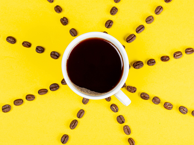 Солнце из чашки кофе с зернами на желтом фоне
