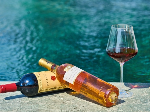 Две бутылки вина и бокал у бассейна