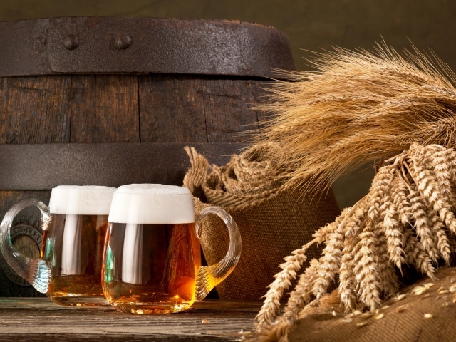 Два бокала пива на столе с колосьями пшеницы  и бочкой