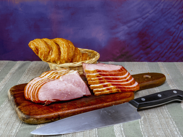 Кусок нарезанной ветчины на доске с круассаном
