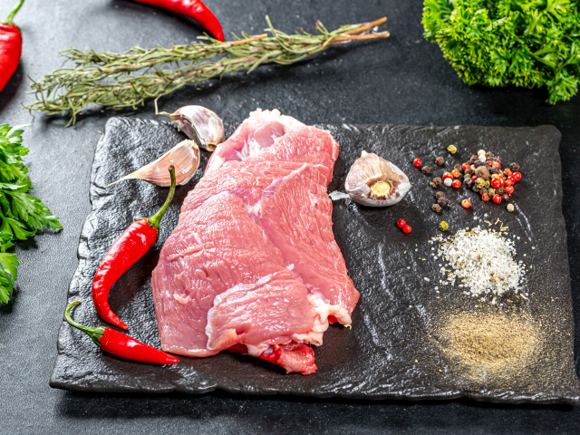 Кусок мяса на столе с острым перцем, чесноком и зеленью