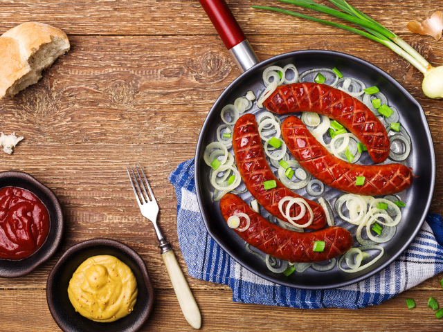 Колбаски барбекю с луком на сковороде на столе с соусом