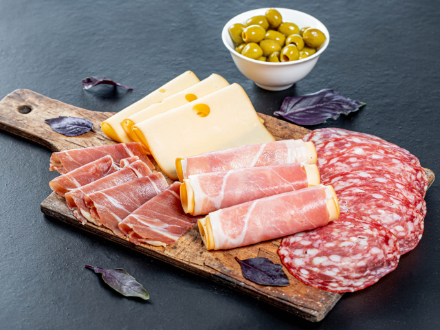 Сыр, бекон и колбаса на разделочной доске на столе с оливками