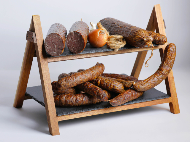 Различные виды колбасы на полке с луком на сером фоне
