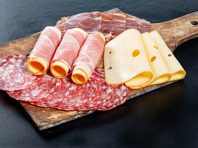 Куски сыра, ветчины и колбасы на доске