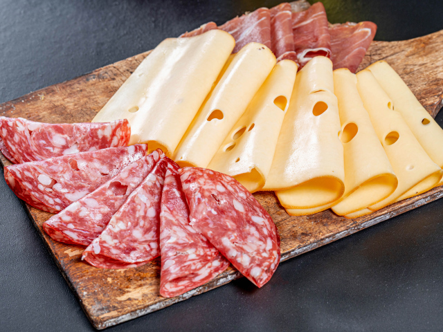 Колбаса, мясо и сыр нарезанный на разделочной доске 