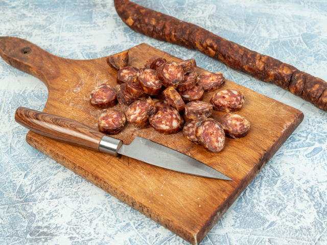 Колбаса нарезана колечками на разделочной доске с ножом 