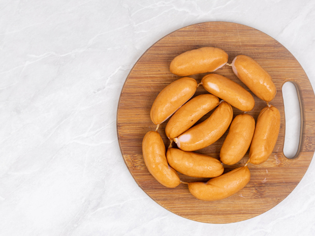 Копченые сардельки на деревянной доске на сером фоне